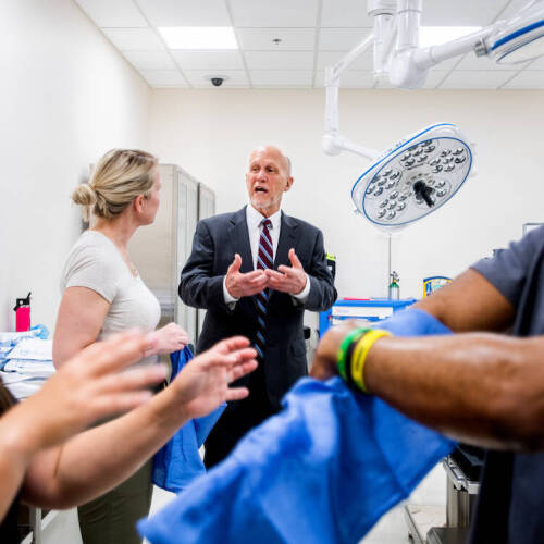 two health professions students in foreground in simulation lab while two faculty talk in the background